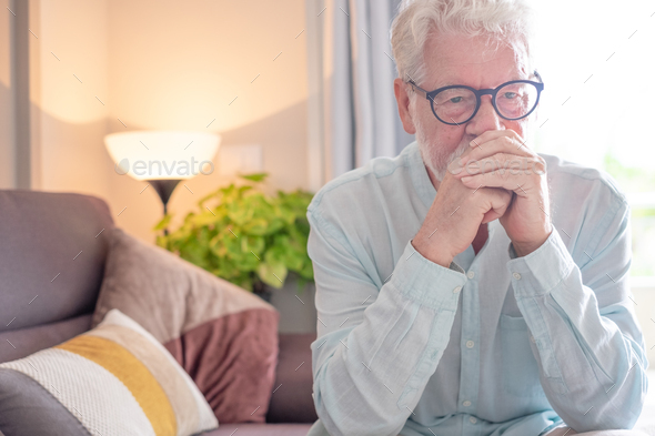 Sad senior man sitting at home alone staring into space, old man suffering from health problems