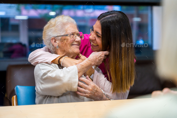 Happy elder woman and nurse embracing in a geriatric