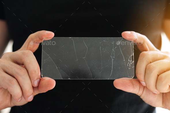Broken protective glass for smartphone touch screen in hands of phone repairman on black background.