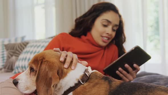 Happy woman lying on sofa using tablet while stroking her dog 4K 4k alt
