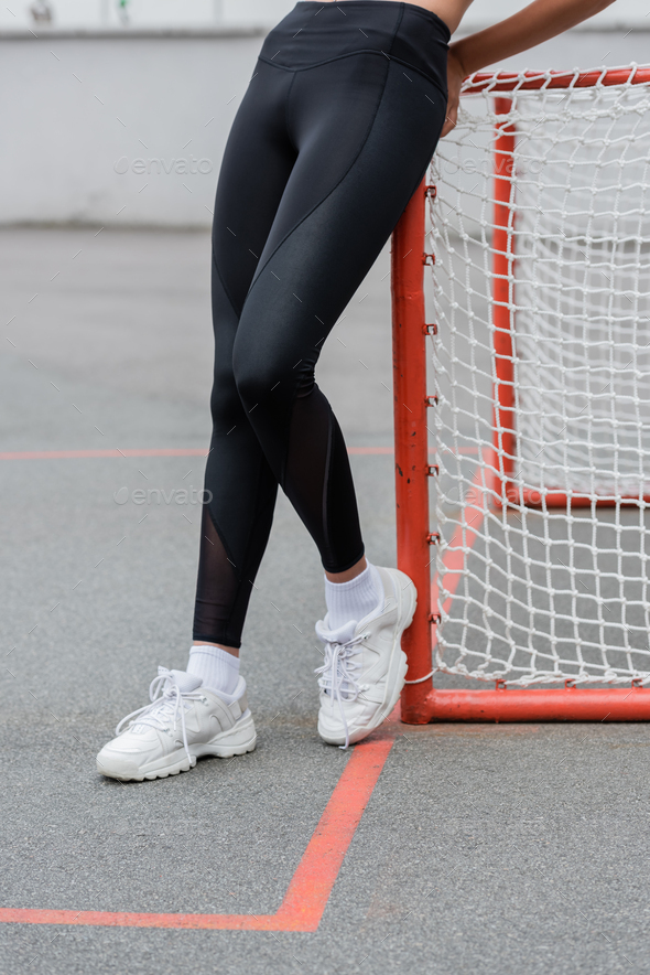 cropped view of african american woman in black leggings and white sneakers  near sports gates Stock Photo by LightFieldStudios