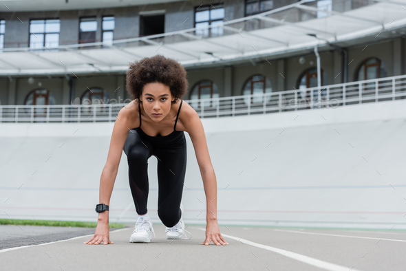 front view of african american woman in sportswear and fitness tracker standing in low start pose