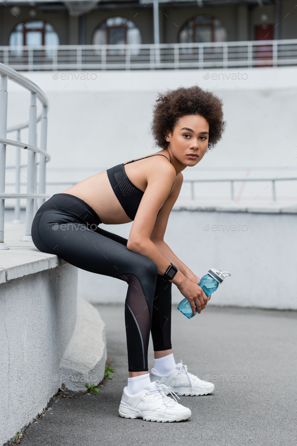 full length of african american woman in black sportswear and white  sneakers sitting with sports Stock Photo by LightFieldStudios