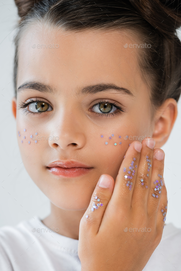 close up of adorable girl with sparkling glitter stars on face looking at camera isolated on