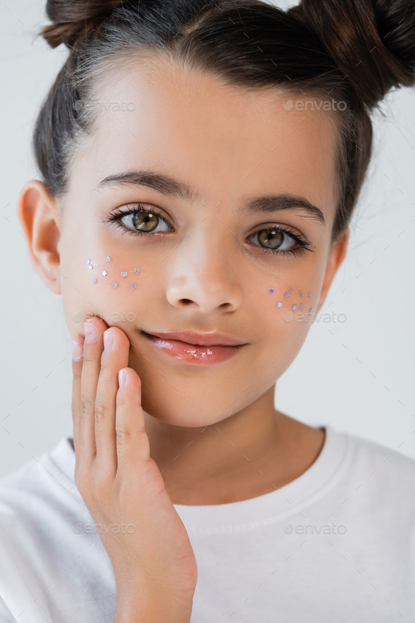 portrait of smiling girl with lip gloss and sparkling glitter stars on face touching cheek