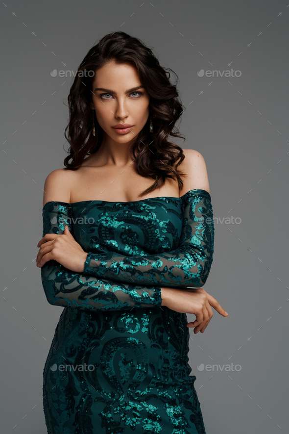 Elegant brunette model in a rich green evening dress on a gray background