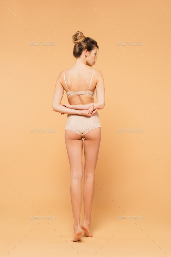back view of barefoot woman with perfect body standing in underwear with  hands behind back on beige Stock Photo by LightFieldStudios