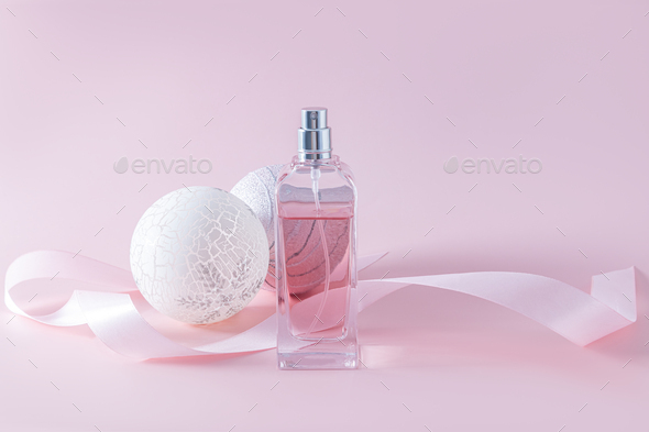 Elegant bottle of women s perfume on pink background among stylish Christmas balls. Presentation