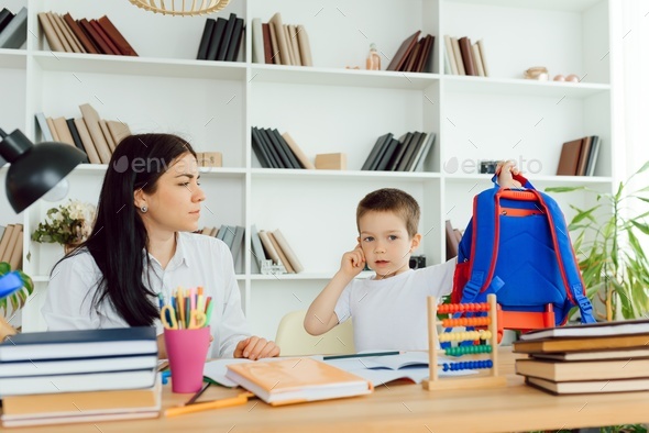 Female private tutor helping young student with homework at desk in bright child\'s room