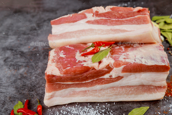 Pork belly meat pieces with hot pepper on grey background