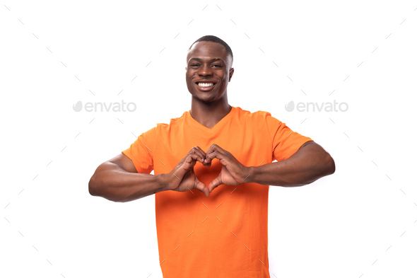 a young american man is wearing an orange t-shirt and showing a heart. corporate clothing concept
