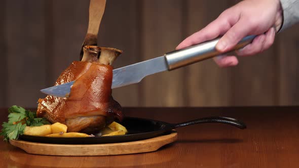 A Man's Hand Cuts a Large Piece of Meat From a Pork Knuckle with a Knife