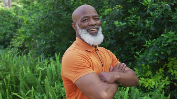 Portrait of african american senior man smiling and crossing his arms in the garden alt