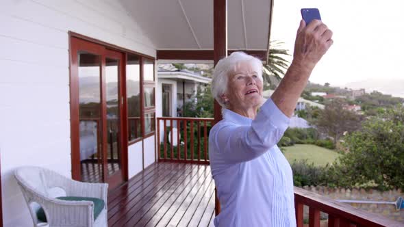 Woman taking selfie with mobile phone in balcony at home 