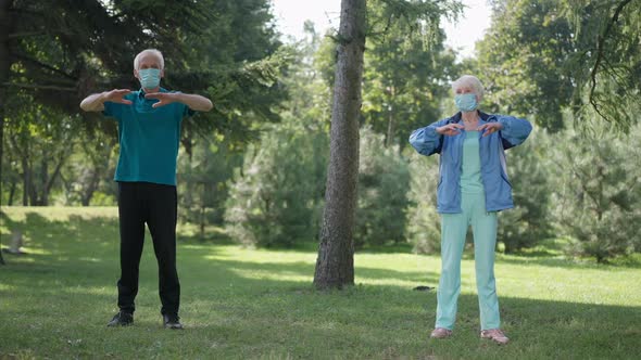 Wide Shot Senior Couple in Coronavirus Face Masks Exercising in Park Warming Up in Slow Motion alt