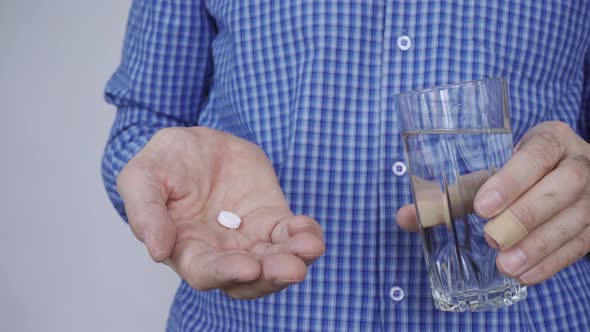 Closeup of a Man's Hands Holding a Glass of Water and a White Round Pill alt