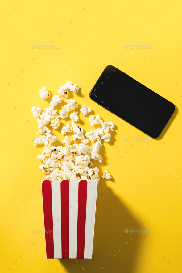 Classic popcorn bucket and smartphone with blank screen on yellow background