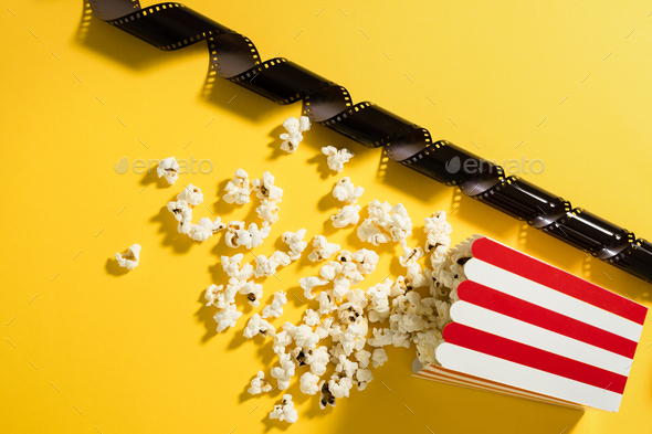 Classic striped bucket with delicious popcorn and film stock on yellow background
