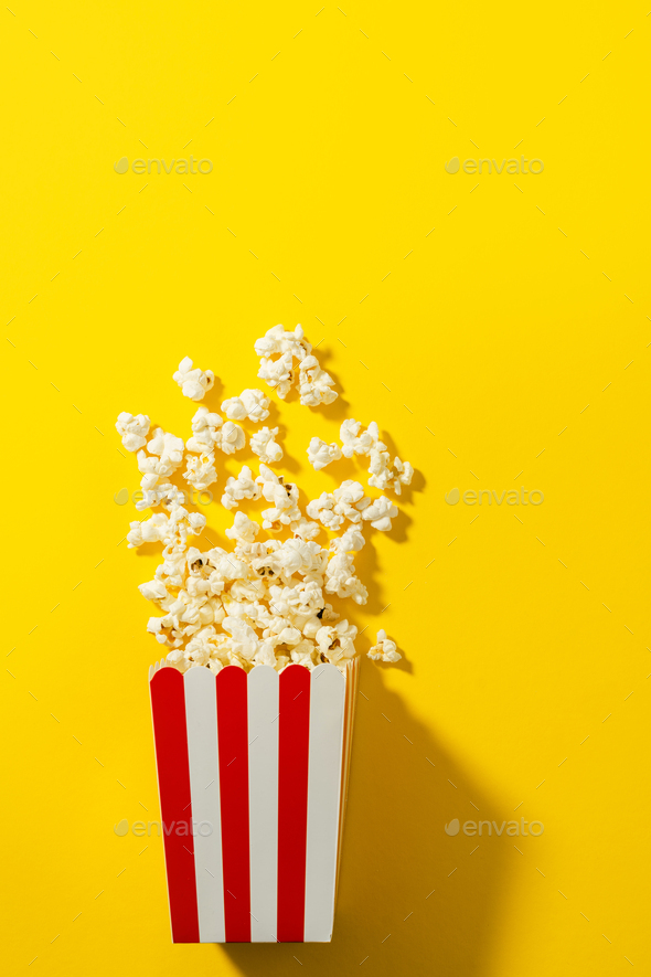 Classic striped bucket with delicious popcorn on yellow background