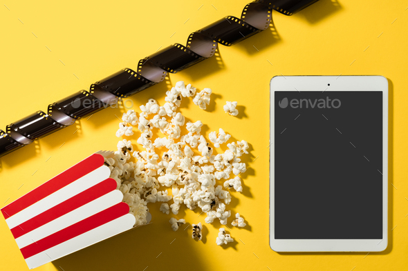 Classic popcorn bucket and tablet computer with blank screen on yellow background