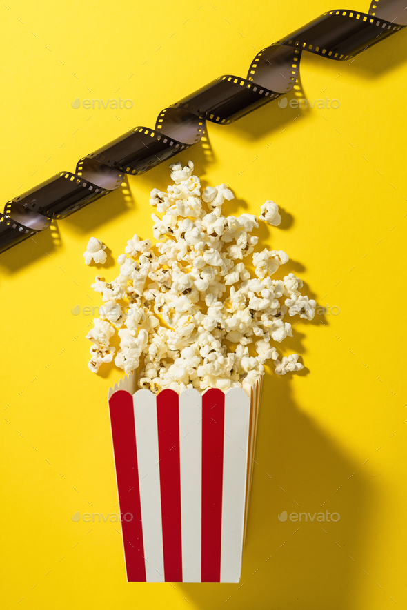 Classic striped bucket with delicious popcorn and film stock on yellow background