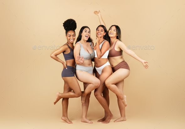 Young diverse women in underwear, embracing on beige background