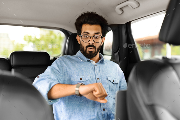 Worried indian entrepreneur sitting in car back seat, checking time