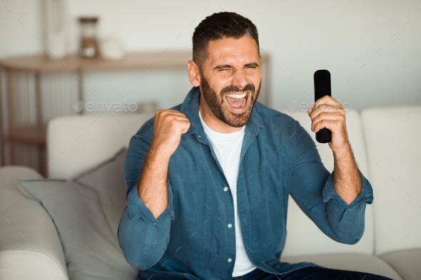Emotional man watching sports on TV celebrating success indoor