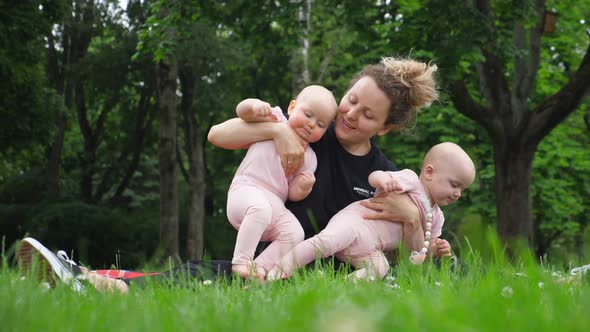 Happy Family Concept. Young Mother Holding Twin Babies In Park.