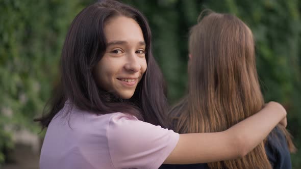Back View Positive Teenage Girl Holding Hand on Friend Shoulder Turning Looking at Camera with alt