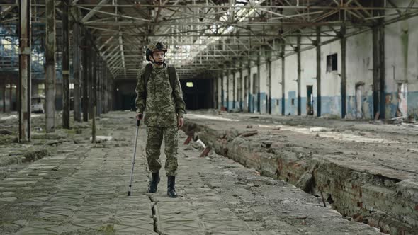 Female Soldier Walking with Crutch Through Destroyed Factory alt