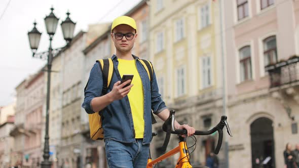 A Young Delivery Man is Going and Texting on a Smartphone alt