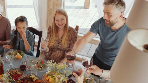 Man Giving Toast and Clinking Glasses with Family Members at Holiday Dinner alt