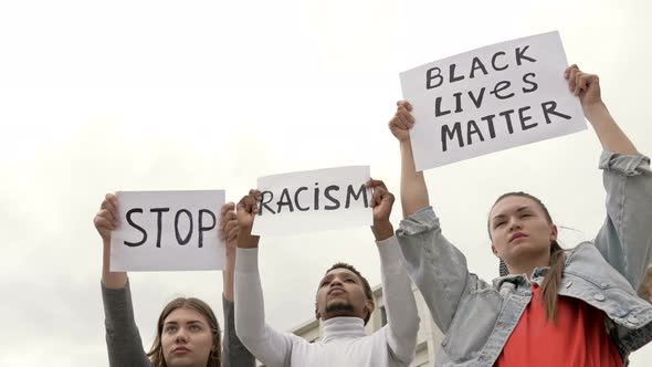 Three Young People of Different Nationalities Protest Against Racial Inequality. They Have Posters alt