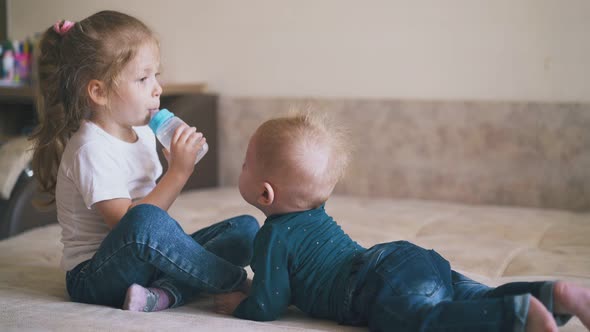 Girl Sucks Teat on Water Bottle and Little Brother on Bed, Stock Footage