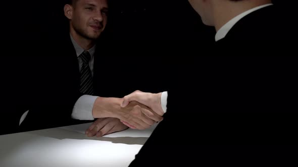Two businessmen making handshake in dark room for illegal deal, white collar crime concept