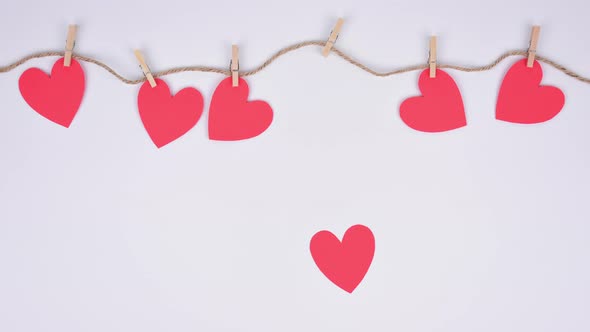 Stop motion red paper hearts fixed with clothespins on a cord. White background. Space for copy.