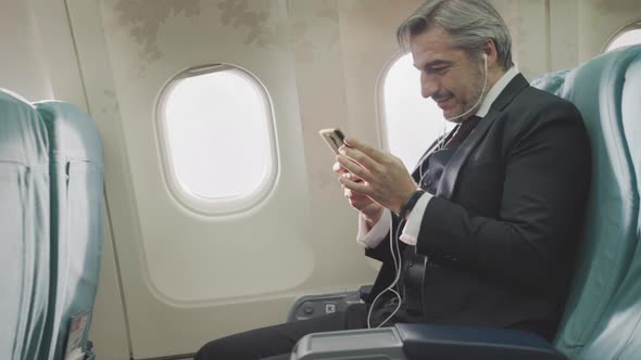 Businessman using mobile phone browsing internet at seat on airplane during flight