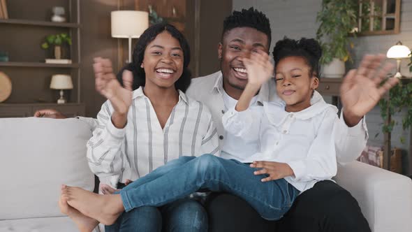 African Family with Daughter Sitting at Home Waving Hands Greeting Look at Camera Talking at Webcam alt
