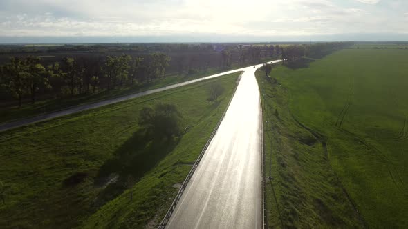 Drone Descends Above Wet Asphalt Road for Cars Between Sown Fields alt