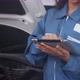 Young woman is mechanic holding tablet computer checking engine of car in the garage. - VideoHive Item for Sale