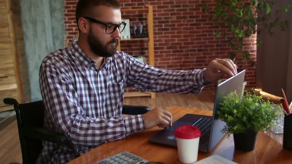 Confident Hipster Man in Wheelchair Finishes Working on Laptop Closes It and Drives Away alt
