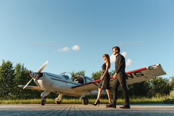 Portrait of two smiling business people, man and woman, walking by plane hangar in airport field