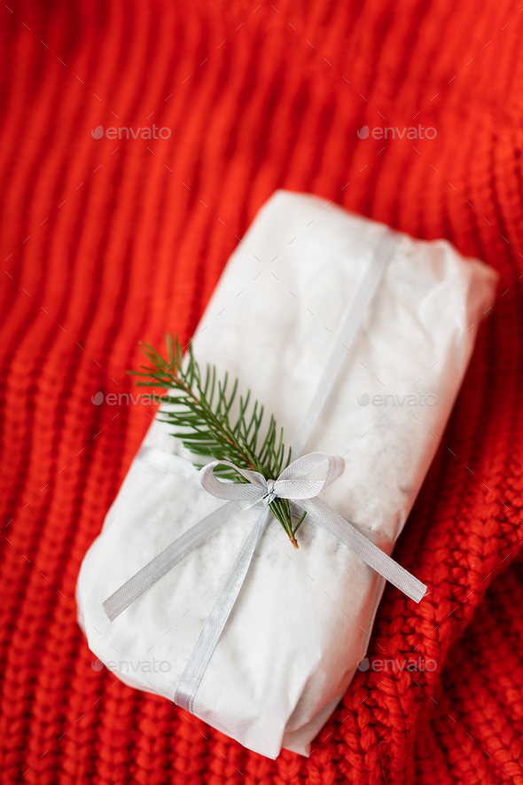 A homemade Christmas stollen sealed in white craft paper lies on a red knitted fabric. Gift wrap.