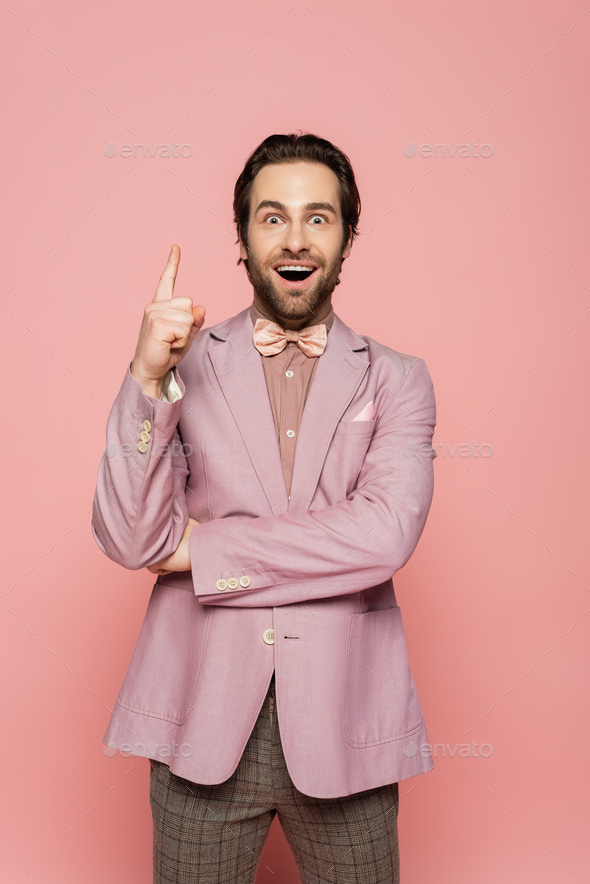 Excited host of event in jacket pointing with finger on pink background