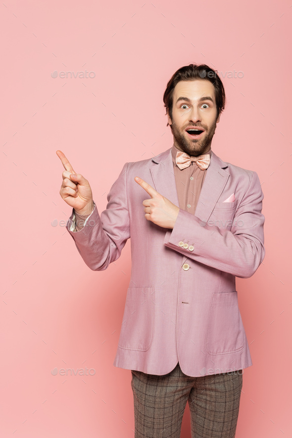 Amazed host of event pointing with fingers on pink background