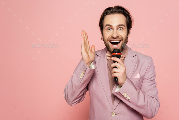 Amazed host of event taking at microphone isolated on pink