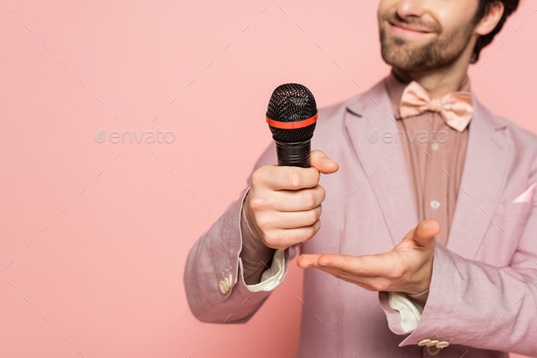 Cropped view of blurred host of event pointing at microphone isolated on pink
