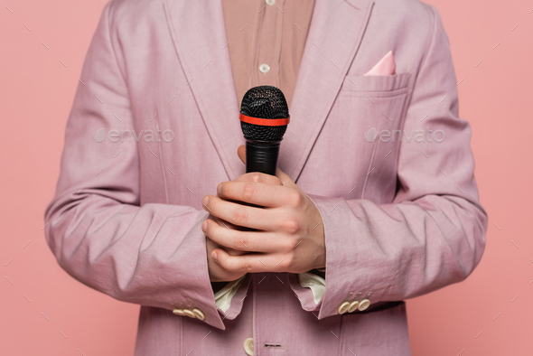Cropped view of host of event in jacket holding microphone isolated on pink
