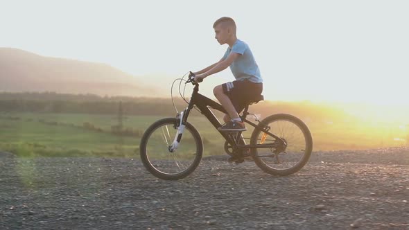 Boy in Blue T-shirt Who Rides a Black Bike in a Mountainous Place at the Summer alt